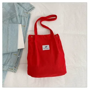 Vista detallada del bolso de pana rojo que resalta la textura de la tela y la etiqueta de diseño