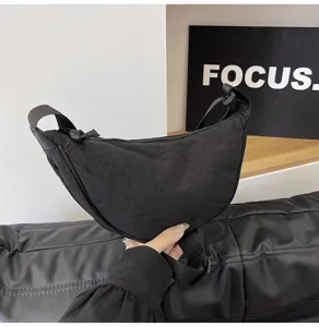 Vista detallada de un elegante bolso de media luna en nailon negro sostenido por una mano