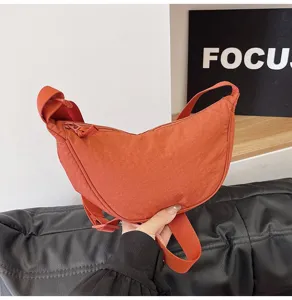 Detalle de un moderno bolso de media luna en nylon naranja con correa de hombro ajustable
