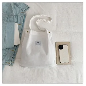Bolso tote de pana blanco minimalista en una cama con accesorios de estilo vida.