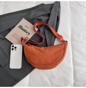 Bolso bandolera de nailon naranja en forma de media luna sobre un blazer gris y tela blanca