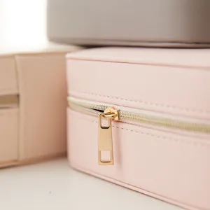 Close-up of a portable pink faux leather jewelry box featuring a golden metal zipper