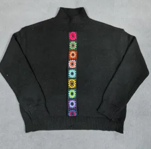Detalle de un suéter negro de mujer con parches de flores de ganchillo de colores vivos.