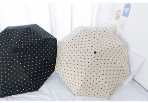 Zwei faltbare gepunktete Regenschirme in Schwarz und Beige auf einem Bett