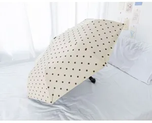 Nahaufnahme eines beigen Automatik-Regenschirms mit braunen Punkten auf einem Bett.