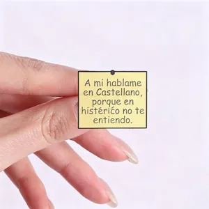 Primo piano di una spilla smaltata quadrata gialla con citazione divertente in spagnolo