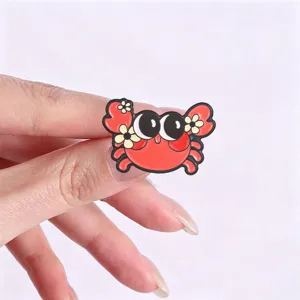 Macro detail of a cute cartoon red crab enamel pin being held to show size and quality.