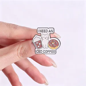 Detailed close-up of a whimsical cat and iced coffee enamel pin held between fingers