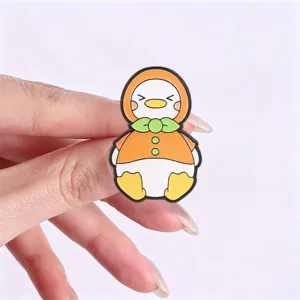 Close-up of a cute orange fruit cartoon duck enamel pin badge held by a hand