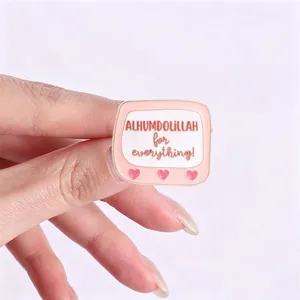 Macro view of a cute pink heart enamel pin featuring Alhumdolillah for everything text