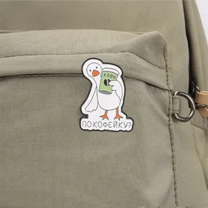 Gros plan d'un pin's en émail humoristique d'oie blanche russe tenant un café sur un sac