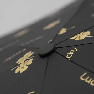 Close-up detail of a premium black folding umbrella featuring golden clover patterns and Lucky text