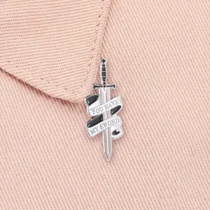 Close-up van vintage zwaardspeld met YOU HAVE MY SWORD lint op roze stof