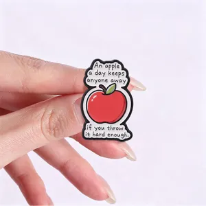 Funny red apple enamel pin with a humorous English quote held by a hand for scale.