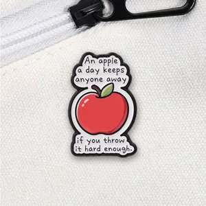 Funny apple enamel pin with humorous English text on a white fabric background.