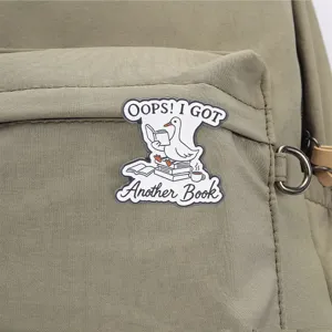 Gros plan d'un pin's en émail avec une oie blanche rigolote lisant un livre sur un sac