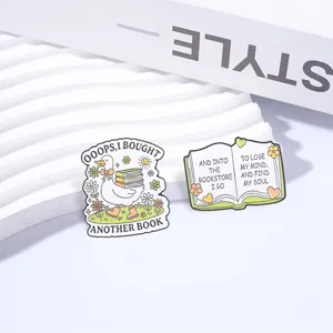 Close-up detail of two book lover enamel pins featuring a cute duck and an open book.