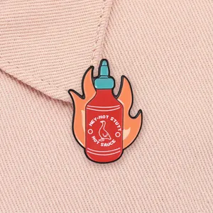 Detailed macro view of a red hot sauce bottle enamel pin with flames on pink denim fabric