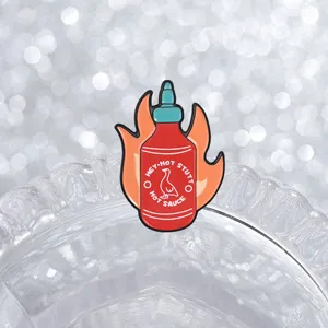 Close-up of a creative hot sauce bottle enamel pin with orange flame background