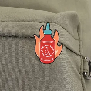 Close-up detail of a funny flame hot sauce bottle enamel pin on green canvas backpack
