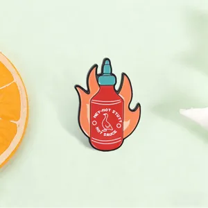 Close-up of a creative hot sauce bottle enamel pin with flames and duck logo.