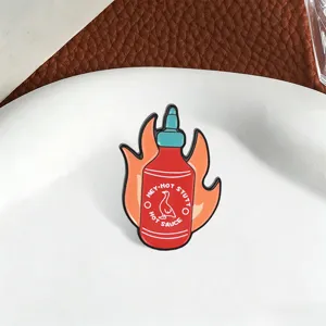Detail shot of a hot sauce bottle enamel pin with a flame background and duck logo