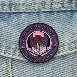Dettaglio della spilla Shadow Daddy Book Club con rosa e ali di pipistrello su tessuto denim