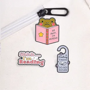 Close-up of reading themed enamel pins featuring a frog and Do Not Disturb signs.