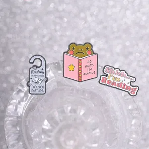 Close-up of frog and book enamel pins for reading lovers, Shhh I'm Reading brooch.