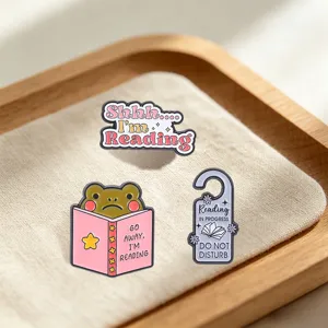 Macro view of reading frog and humorous text enamel pins on a cream fabric tray