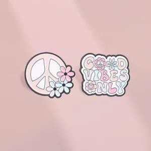 Detailed macro view of pink hippie peace sign and 'Good Vibes Only' enamel flower brooches.