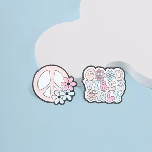 Close-up detail of pastel pink peace sign and Good Vibes Only enamel pins with flowers