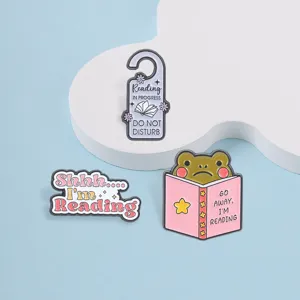 Funny enamel pins for book lovers featuring a reading frog and do not disturb text.