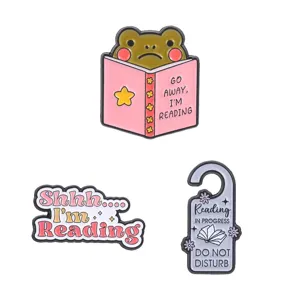 Set of three creative enamel pins for book lovers featuring frog and reading themes