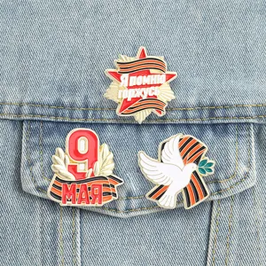 Detailed view of three Russian Victory Day enamel pins pinned on denim jacket fabric.