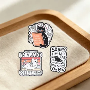 Detail of three funny cat enamel pins featuring humorous English quotes on a fabric