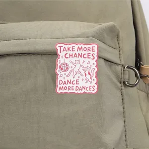 Close-up of dancing cats enamel pin with motivational text on a green backpack