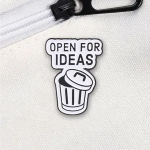 Close-up detail of a funny 'Open For Ideas' trash can enamel pin on a white canvas bag