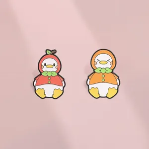 Detailed macro shot of cute apple and orange fruit duck enamel pins on a soft pink background