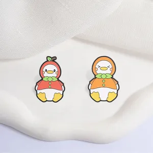 Detailed view of two cute cartoon duck enamel pins in apple and orange outfits.