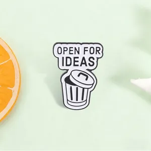 Detailed macro shot of a funny metal pin featuring a trash can and 'Open For Ideas'