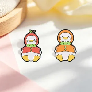 Detailed macro shot of cute apple and orange fruit duck enamel pins on fabric background