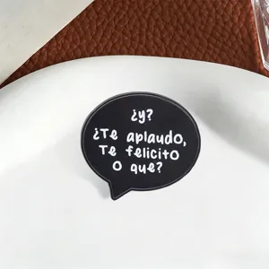 Detailed macro view of a black enamel brooch in speech bubble shape with Spanish text