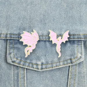 Close-up detail of two pink dragon enamel pins pinned onto a blue denim jacket pocket.
