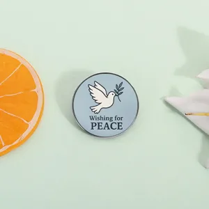 Dettaglio di una spilla rotonda in metallo con colomba della pace e scritta 'Wishing for PEACE'