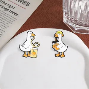 Detailed shot of two cute cartoon white goose enamel pins drinking juice on a plate