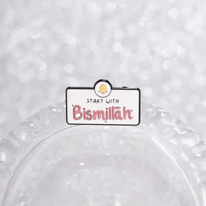Detailansicht der weißen Emaille-Bismillah-Brosche mit rosa Text und gelber Glocke