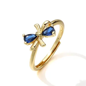 Elegante anello a fiocco dorato con pietre blu a goccia, design aperto regolabile.