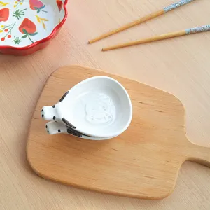 Close-up detail of cute ceramic animal sauce dish showcasing embossed cow design on wooden board.