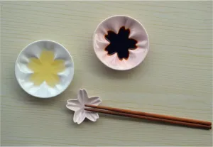 Detailed close-up of ceramic cherry blossom dipping dish and wooden chopstick set.
